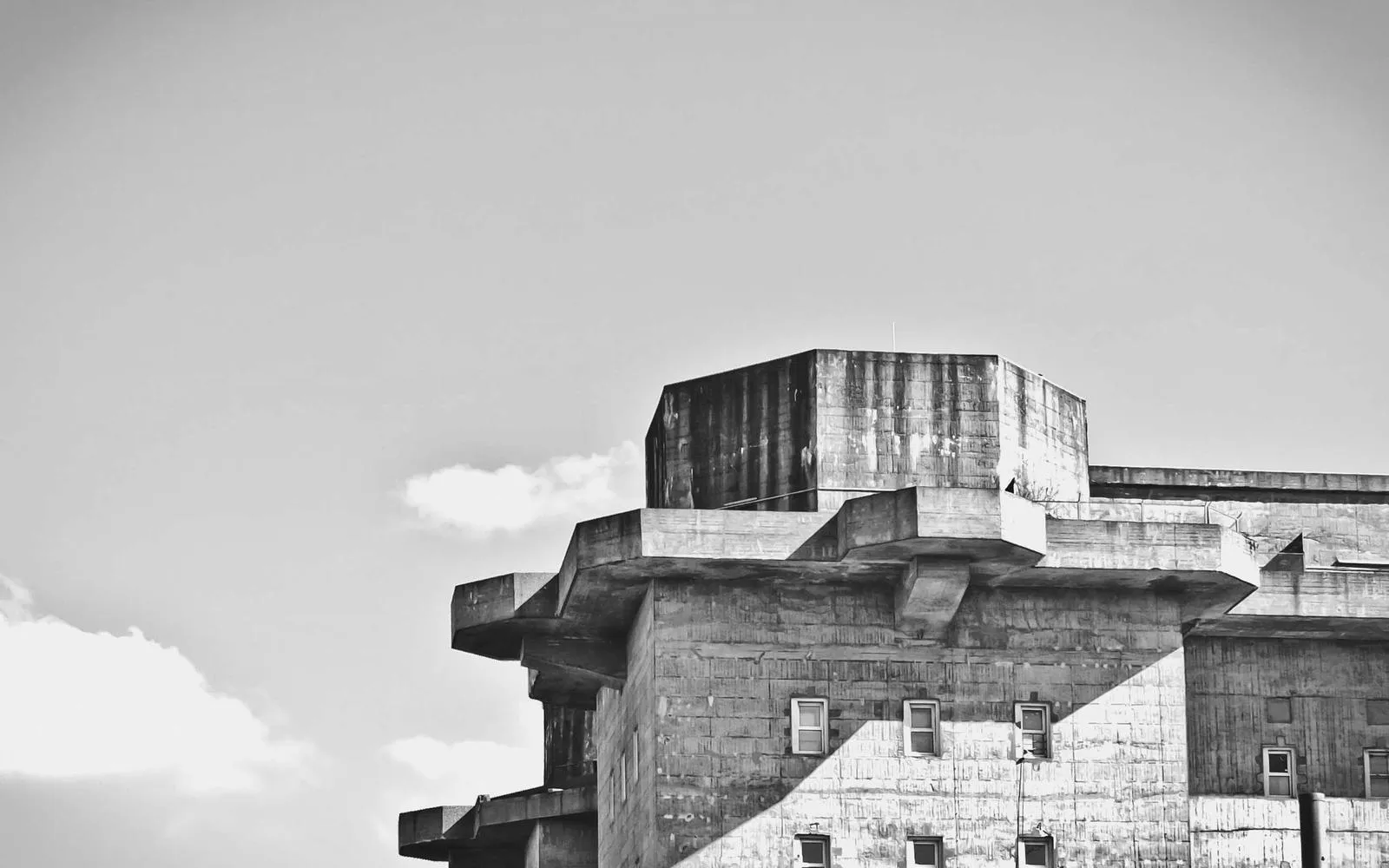 A plain concrete building against a pale sky, in black and white